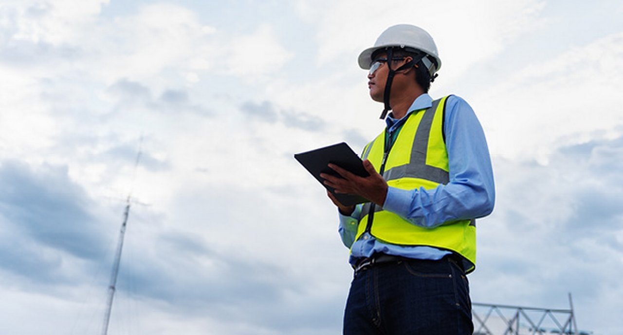 Worker wearing a white hardhat carrying a clipboard