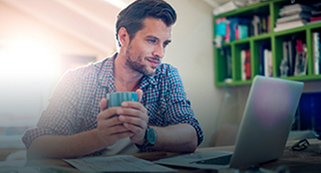 A young man in front of his laptop holding a cup in his hands