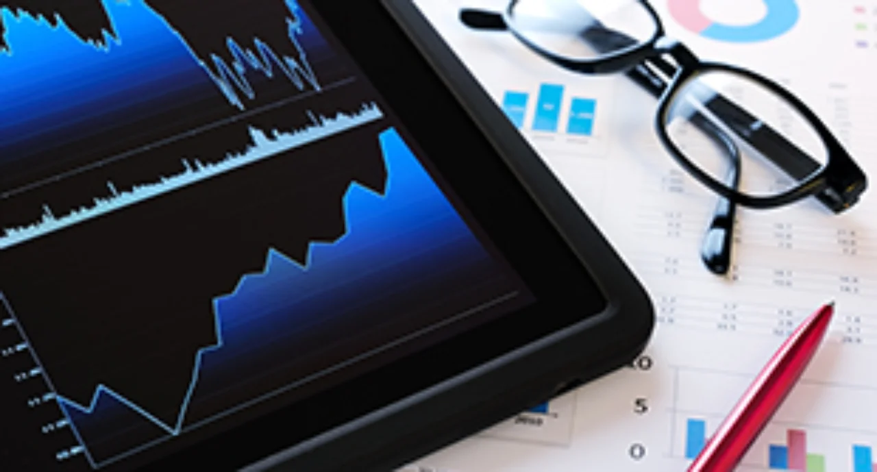 glasses between spreadsheets and a tablet showing share price graphics