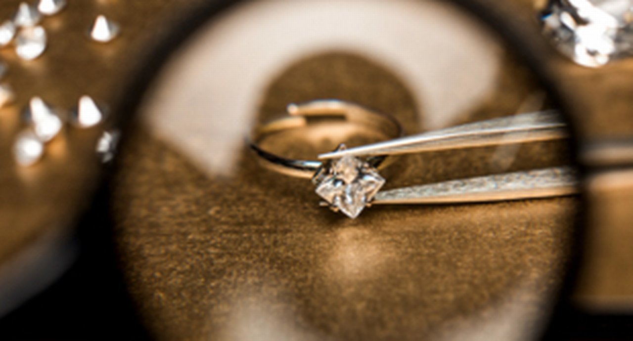 A diamond in tweezers viewed through a magnifying glass