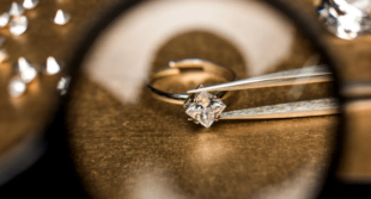 A diamond in tweezers viewed through a magnifying glass