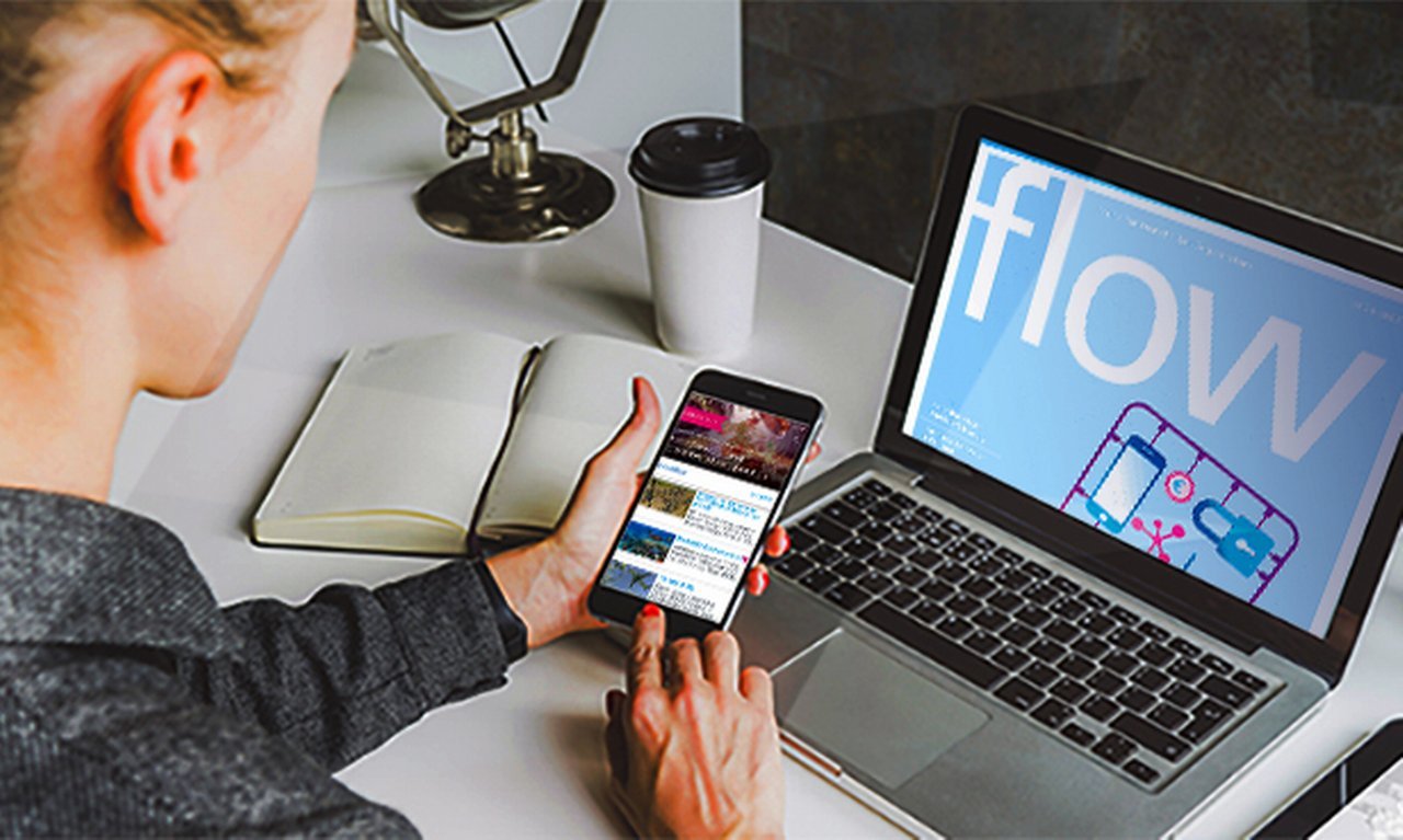 A woman holding a smartphone next to a laptop with flow magazine logo