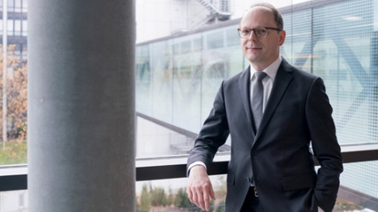 man in business dress code next to a concrete pillar in front of a glass wall