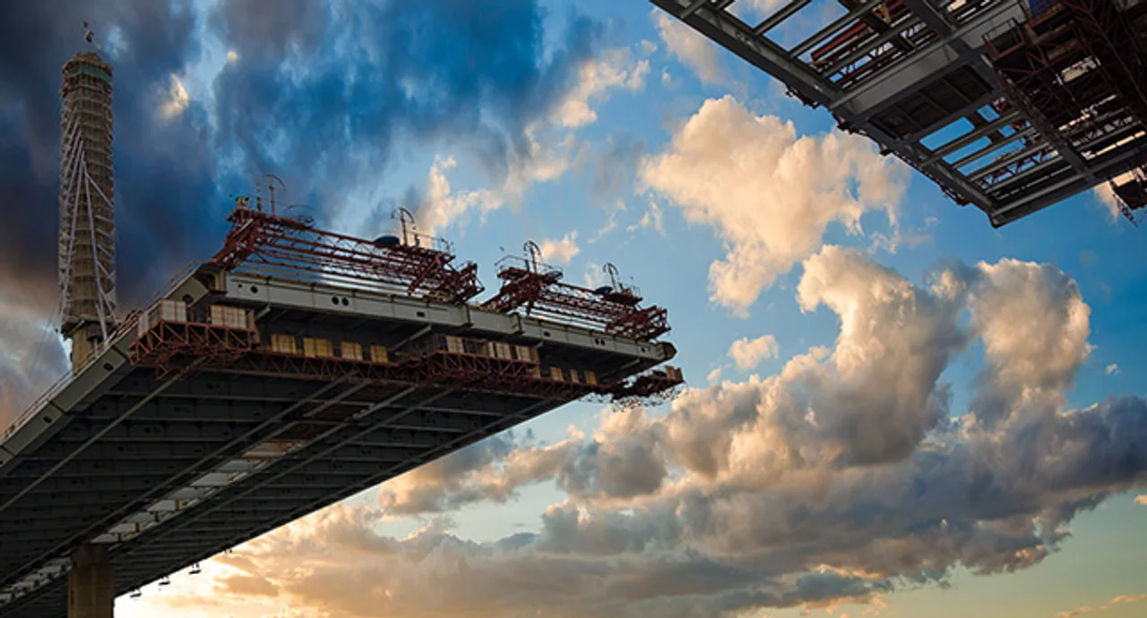 Steel platform of a bridge under construction, cantilevered against a cloudy sky at sunset