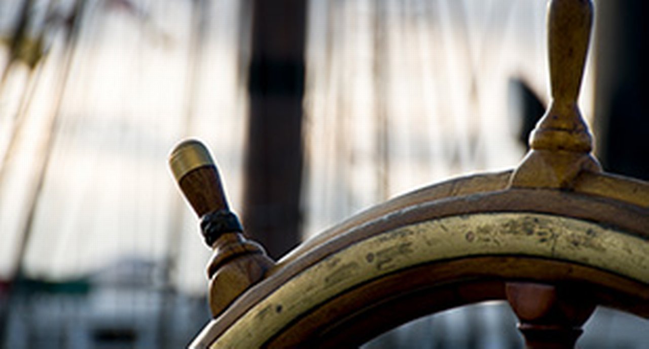 top part of a ship's wheel in front of a blurry boat