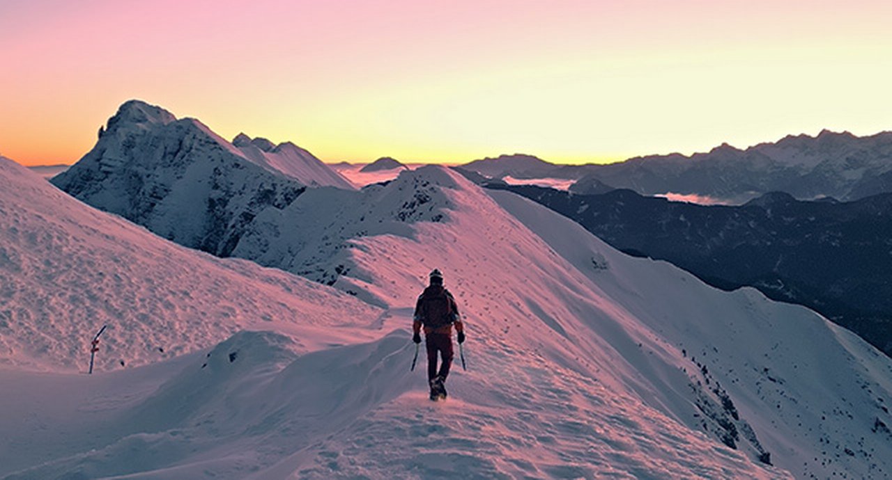 Hiker treks up a snowy mountain slope at sunset, symbolizing perseverance and the beauty of nature's journey.