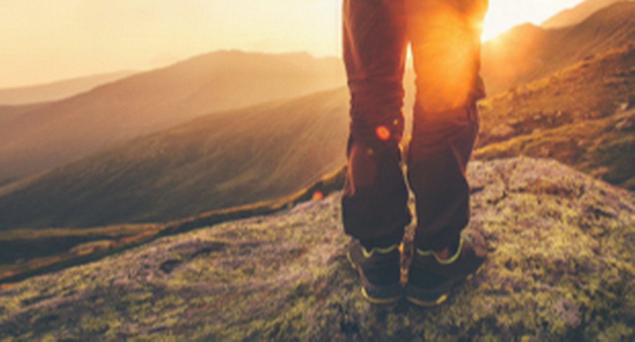 A hiker overlooking a mountainous valley against the setting sun