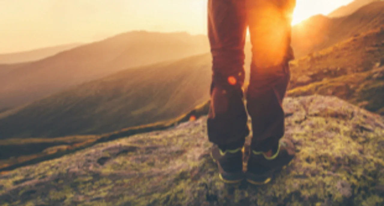 A hiker overlooking a mountainous valley against the setting sun