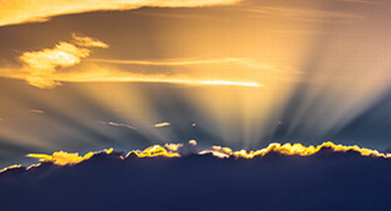 The sun shining behind dark clouds ready to break through