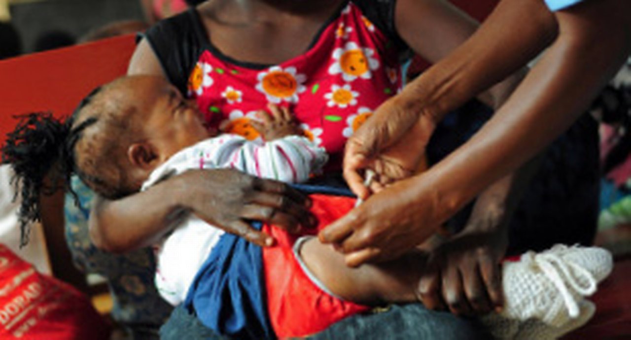 A young woman holding here baby which is being injected with medicine