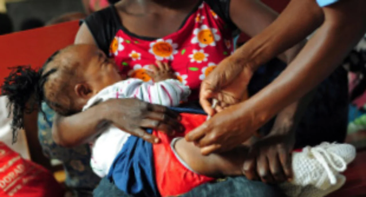 A young woman holding here baby which is being injected with medicine