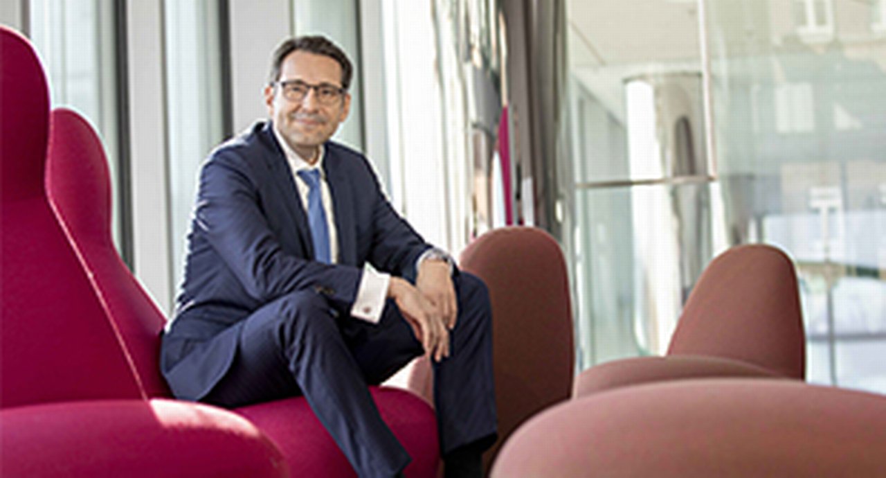 Jörg Bermüller, Head of Cash and Risk Management in Group Treasury, Merck sitting on a red chair in a glass building