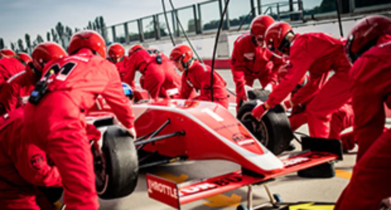 Pit crew in red uniforms changing tires on formula race car during pit stop