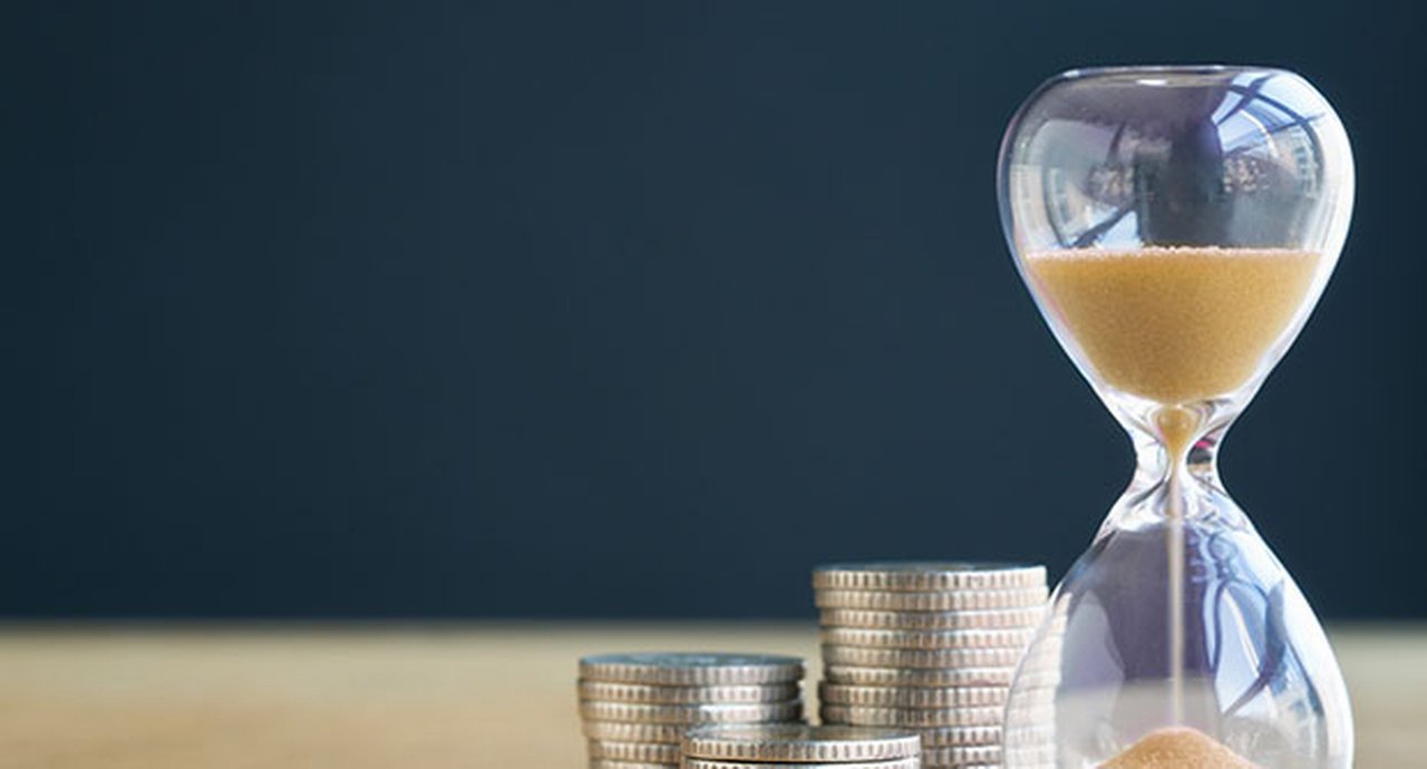Sand hourglass next to stacked coins