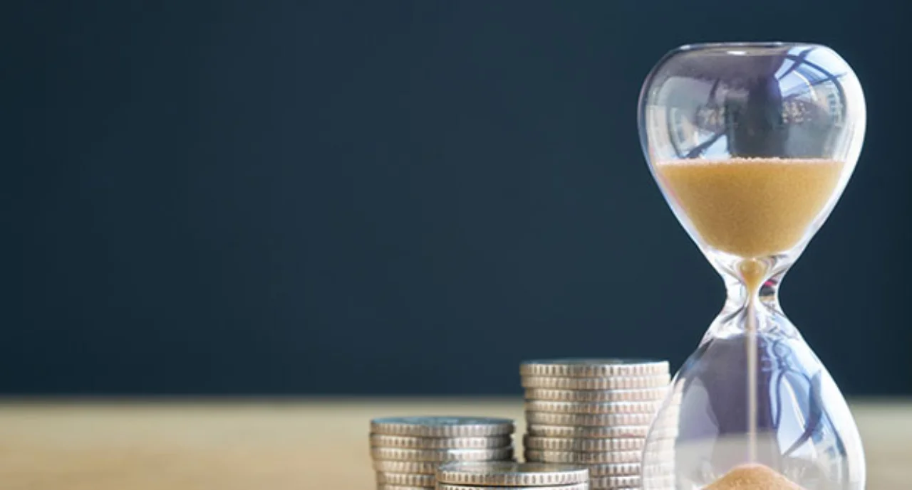 Sand hourglass next to stacked coins
