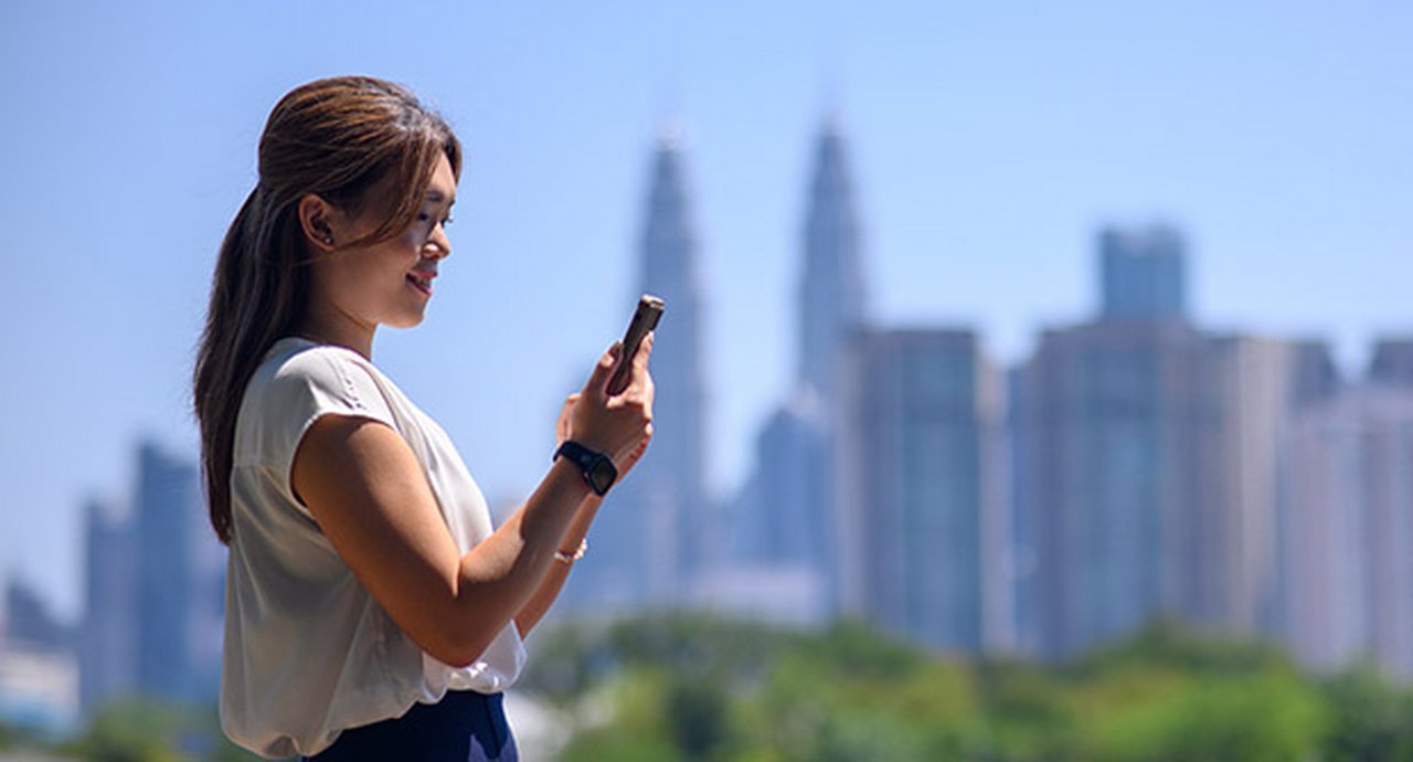 Asian woman holding her phone before a skyline