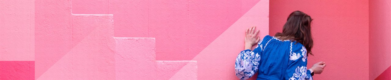 Woman in front of abstract pink background peeks around the corner