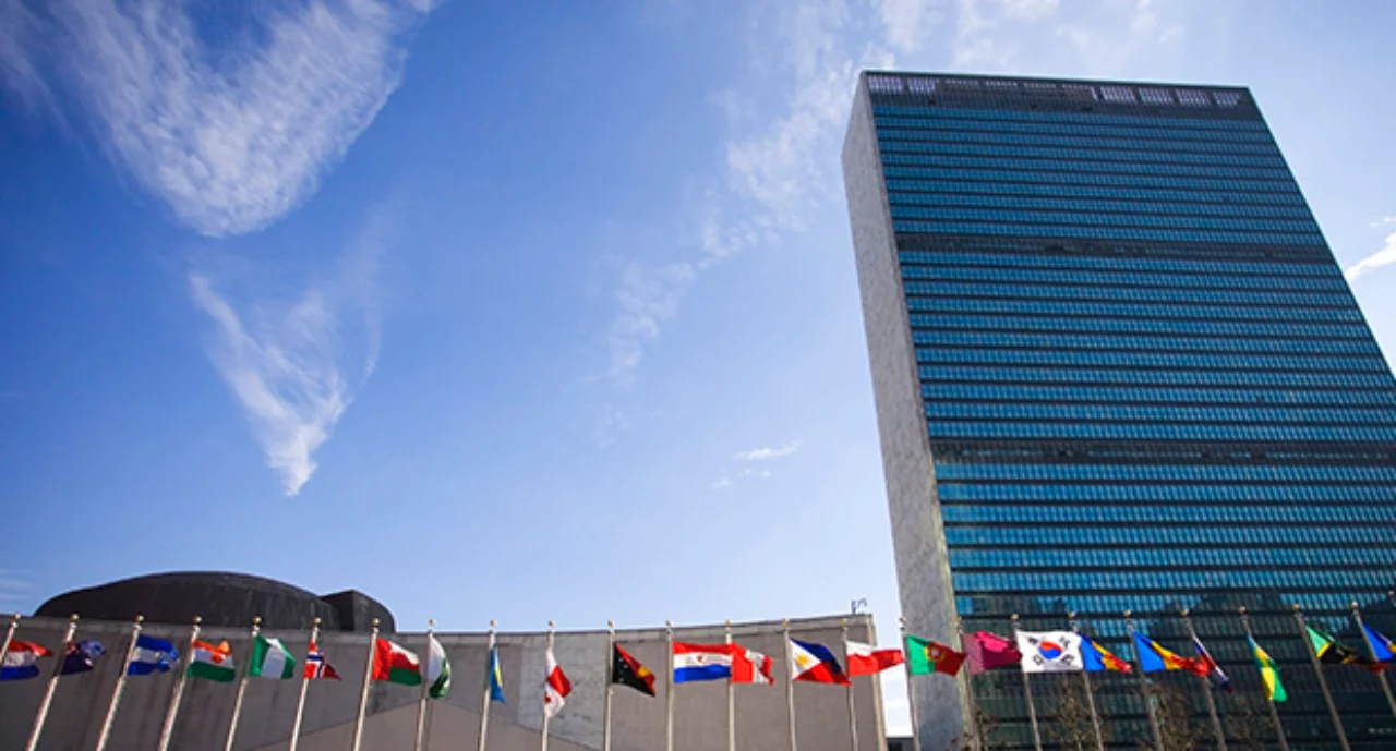 Colorful flags of the world waving in the wind in front of the United Nations building.