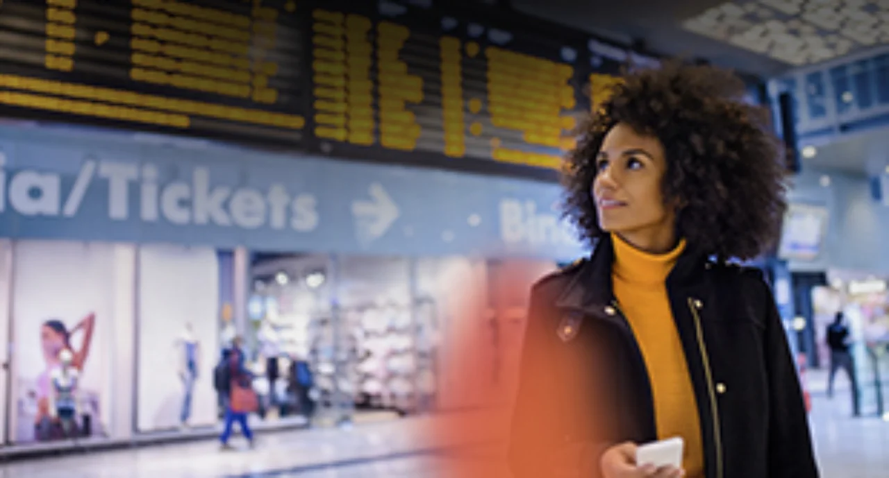 A young woman in front of an airport terminal looking upwards away from her smartphone