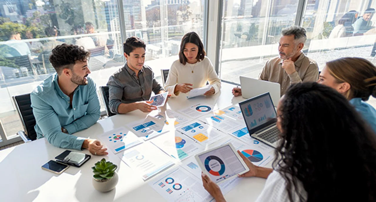 People in an internal business meeting reviewing documents with readable financial data, graphs, and charts