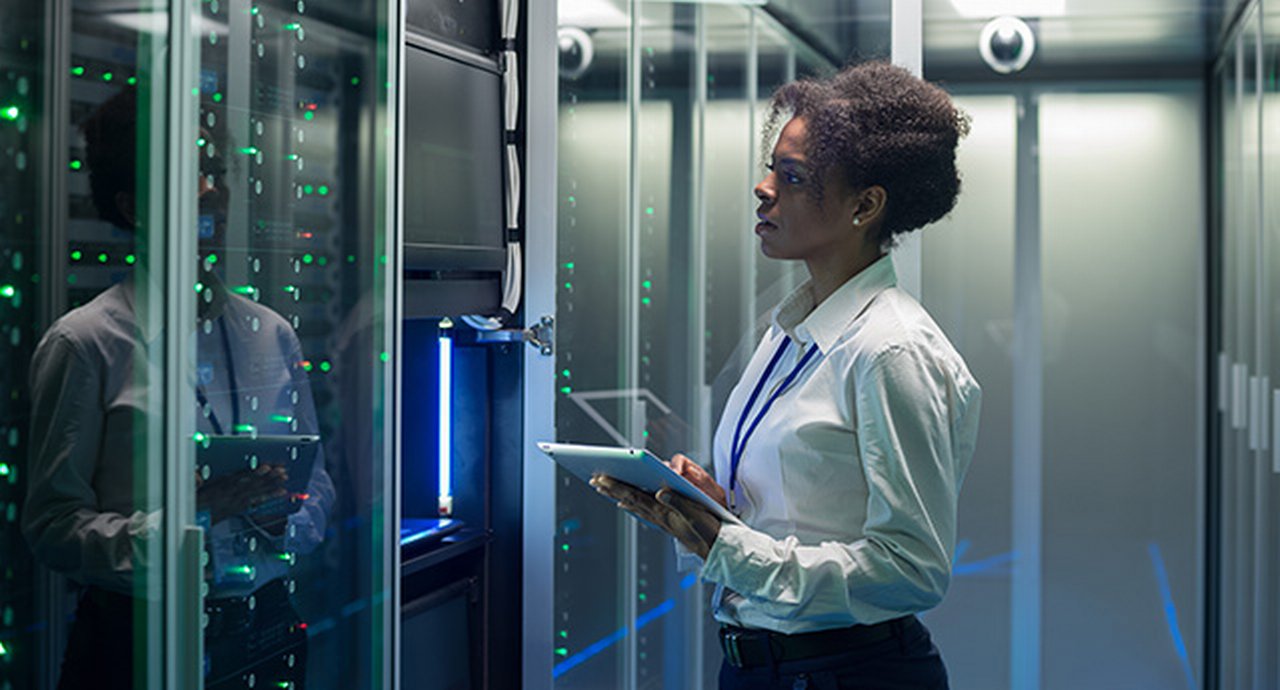 Medium shot of female technician working on a tablet in a data center full of rack servers running diagnostics and maintenance on the system