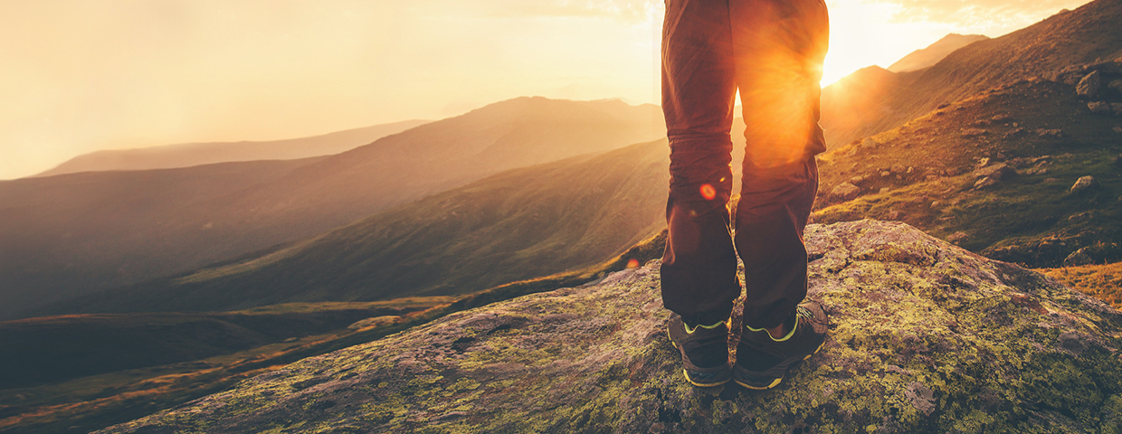 A hiker overlooking a mountainous valley against the setting sun