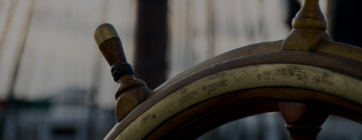 top part of a ship's wheel in front of a blurry boat