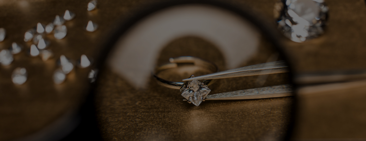 A diamond in tweezers viewed through a magnifying glass