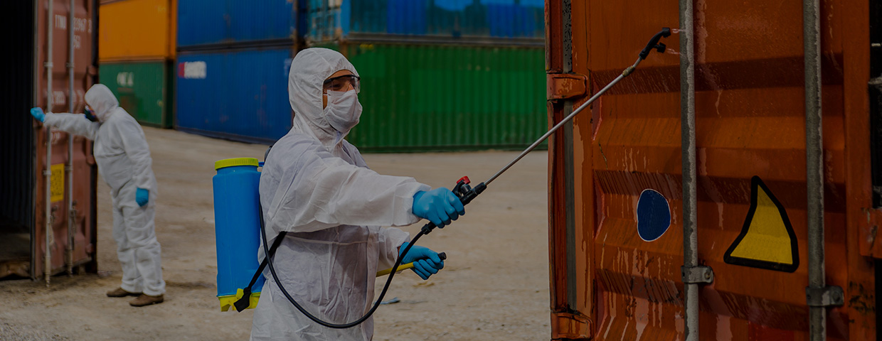 A technician in a Hazmat suit disinfects a shipping container