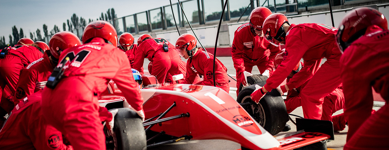 Pit crew in red uniforms changing tires on formula race car during pit stop