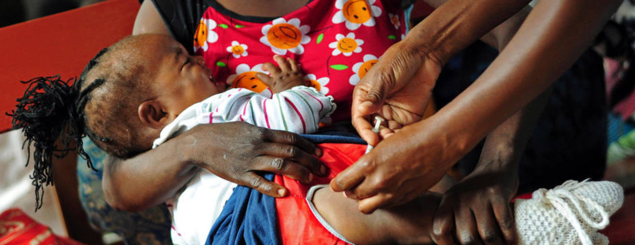 A young woman holding here baby which is being injected with medicine