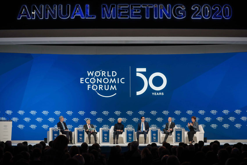 six people sitting on chairs on a stage with blue background, where world economic forum 50 years is written