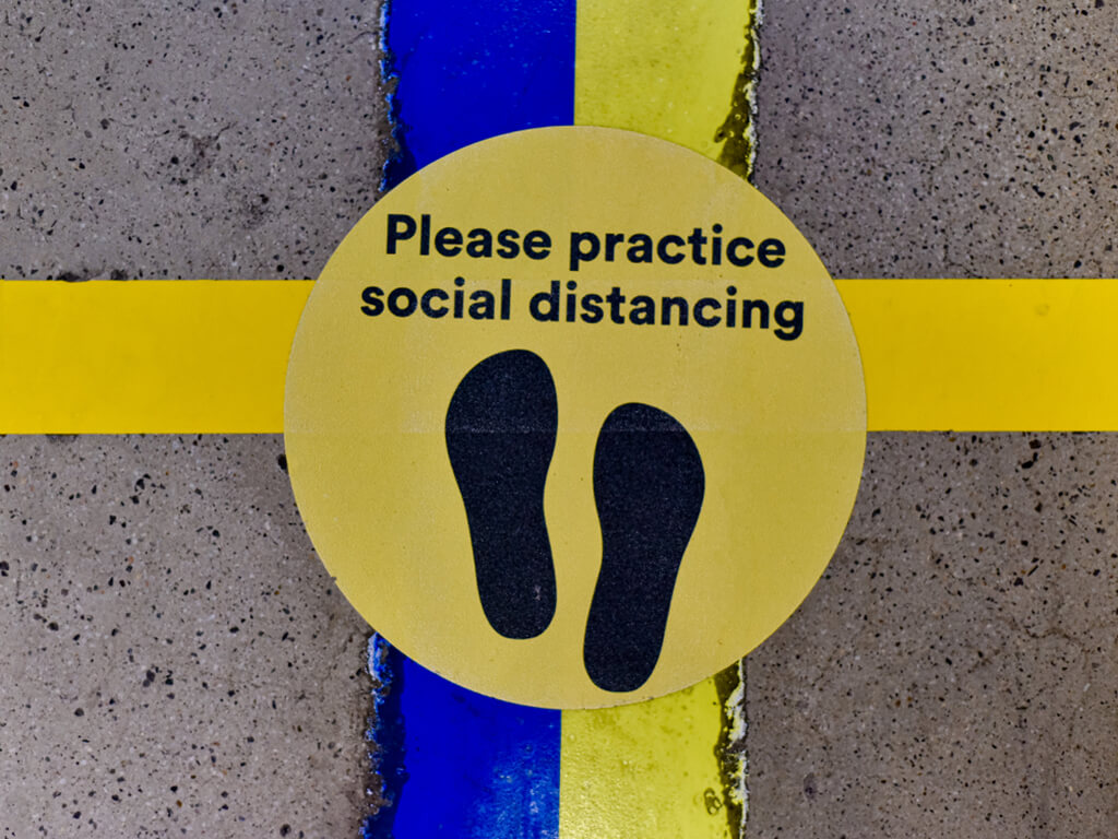 walkway with yellow and blue line and yellow dot on it. black text please practice social distancing